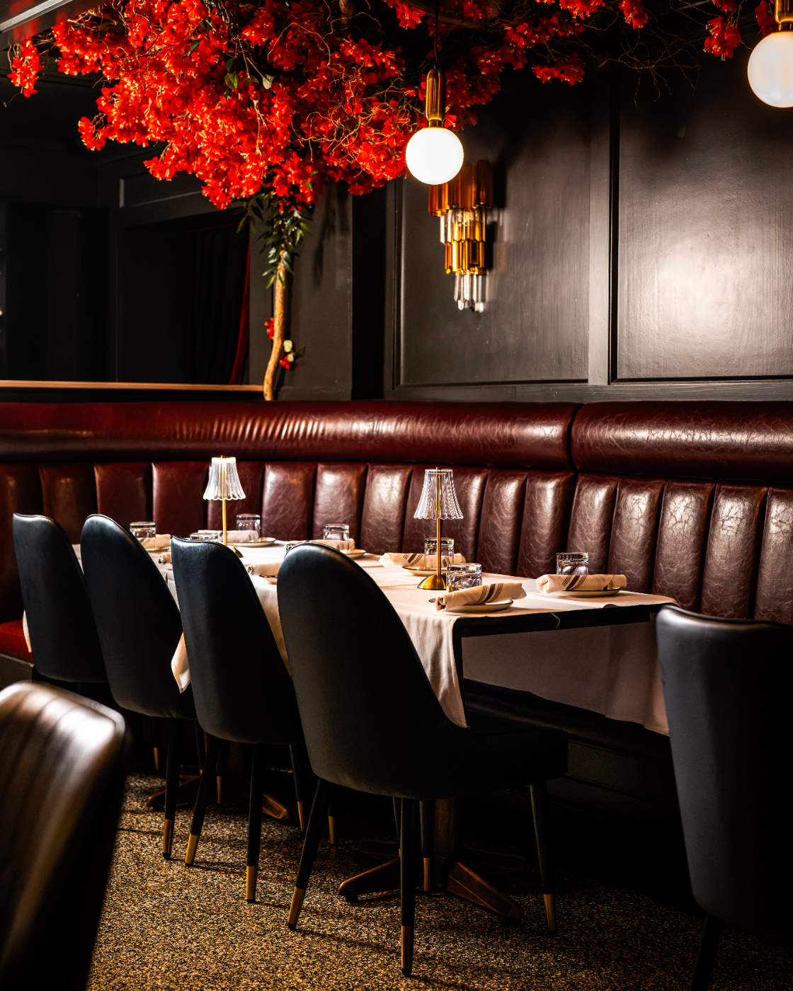 A booth wrapped in red blossoms, set for dinner