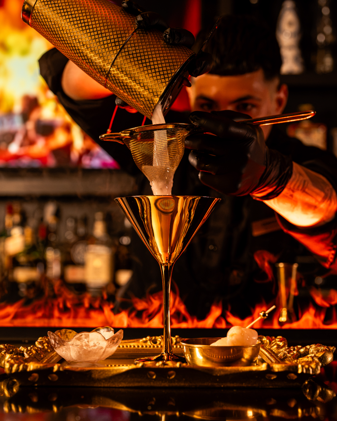 Our bartender straining a golden cocktail over open flames