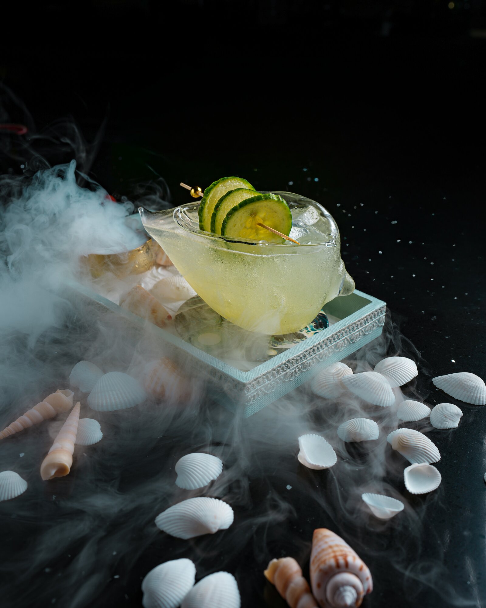A smoking cucumber cocktail served in a seashell glass